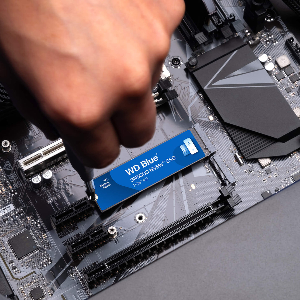 WD Blue SN5000 500GB NVMe PCIe 4.0 SSD — being fitted into an M.2 slot by hand