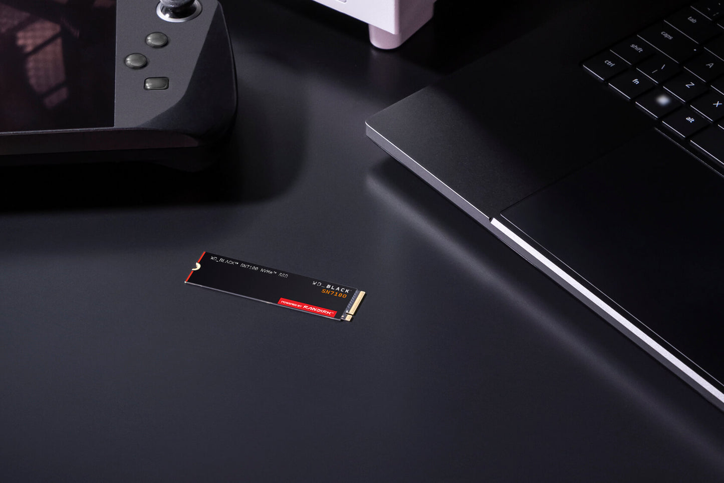 WD_BLACK SN7100 1TB NVMe SSD — shown on a desk beside a handheld console