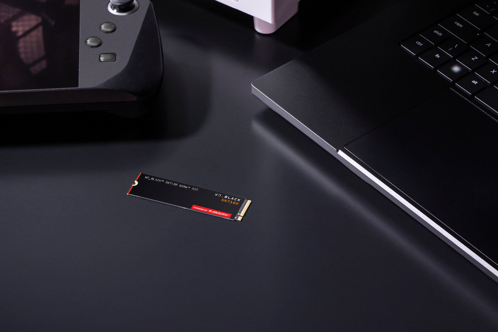 WD_BLACK SN7100 1TB NVMe SSD — shown on a desk beside a handheld console